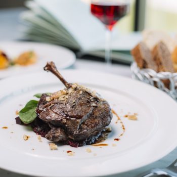 top view of duck leg cooked in sauce garnished with spinach and walnut